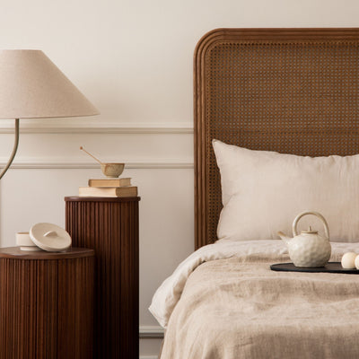 Bedroom with medium brown wicker headboard and light beige sheets. Two medium brown wood accent tables and light beige lampshade. Wall has wainscotting painted in Crisp Muslin