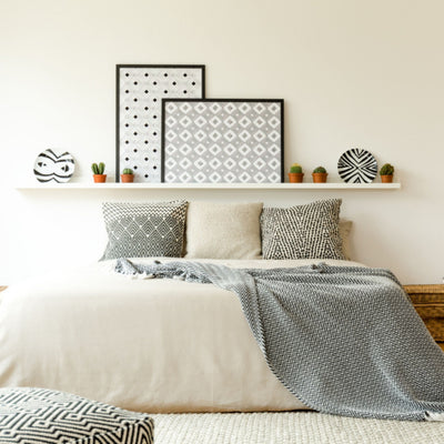 Bedroom with eclectic patterned pillows with light cream bedding. Shelf with eclectic art with wall painted Glisten Green