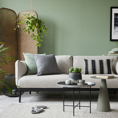 Living area with grey sofa with black hardware and complimentary accent tables, wicker divider and greenery. Wall painted in Cloistered Garden