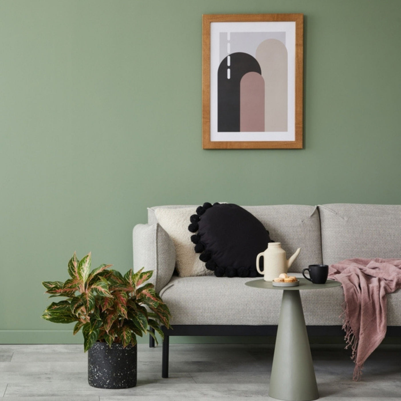 Living area with light gray sofa, round pillow, pink throw blanket and a small accent table. Wall painted in Cloistered Garden