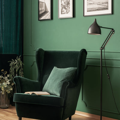 Sitting area with green velvet wingback chair with light flooring. Wall color painted in Forest Path color