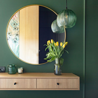 Hung shelf with drawers, round mirror with gold frame and clear green glass with botanical leaf patterned pendant light. Wall color Green Bayou