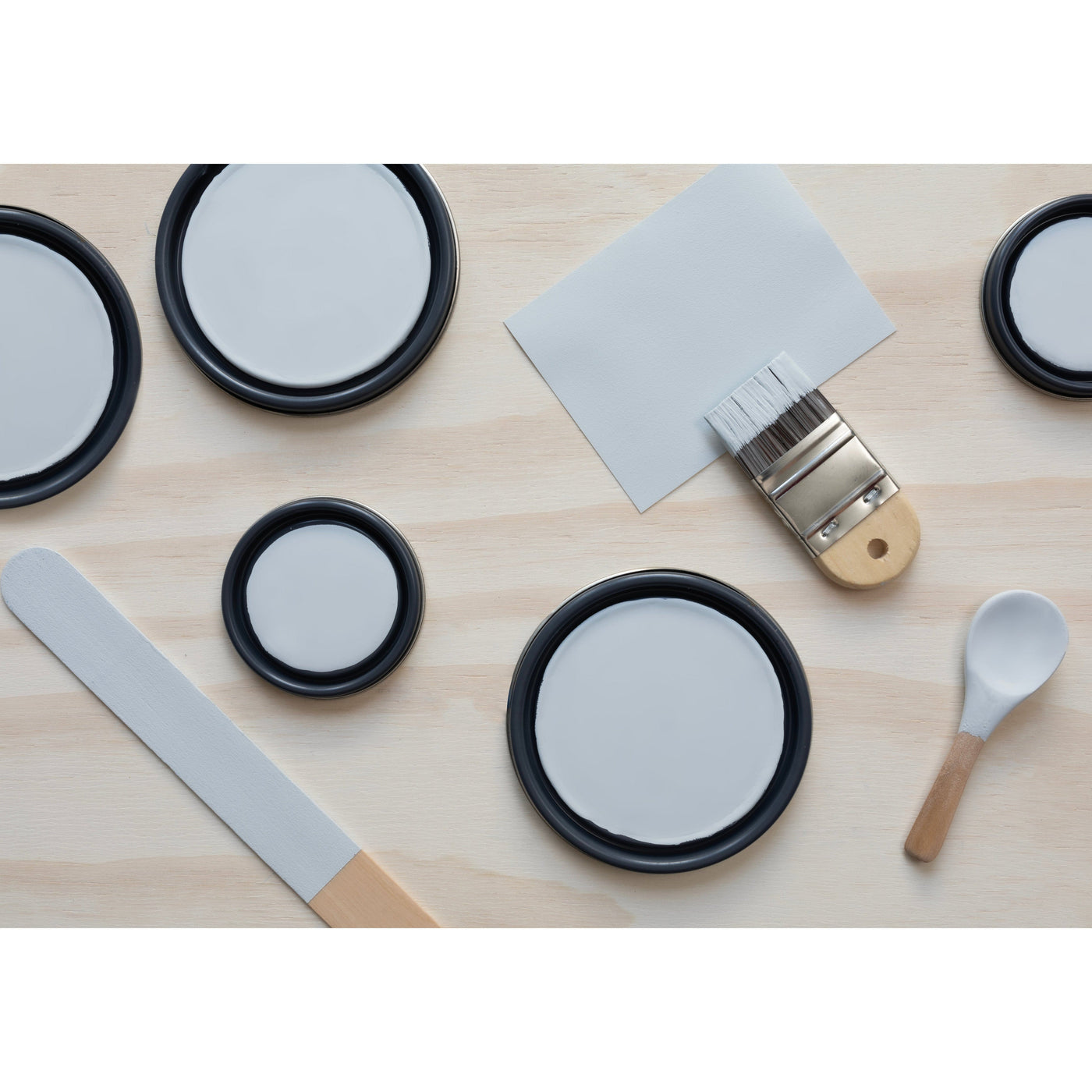 flatlay with paint lids, small paint brush, wooded spoons and rounded sticks painted in Cold Water