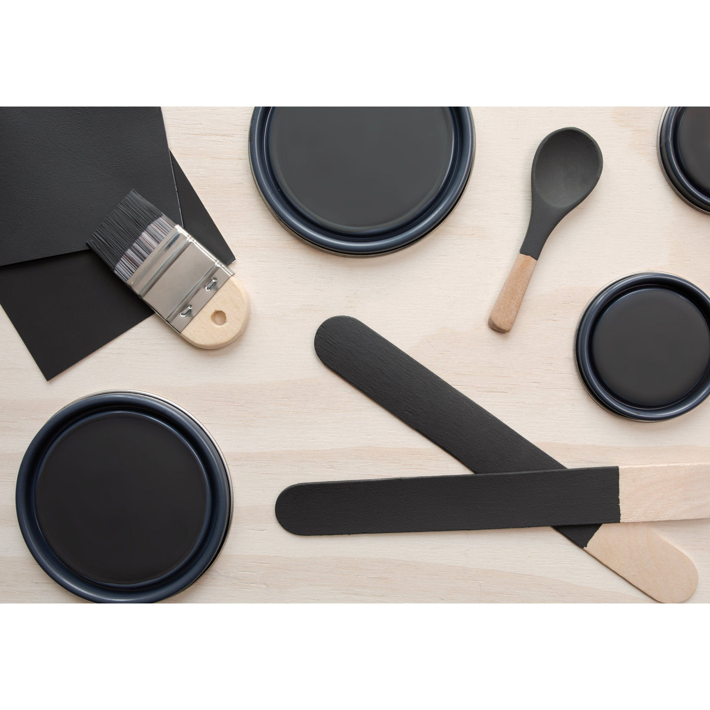flatlay with paint lids, small paint brush, wooded spoons and rounded sticks painted in Blackjack