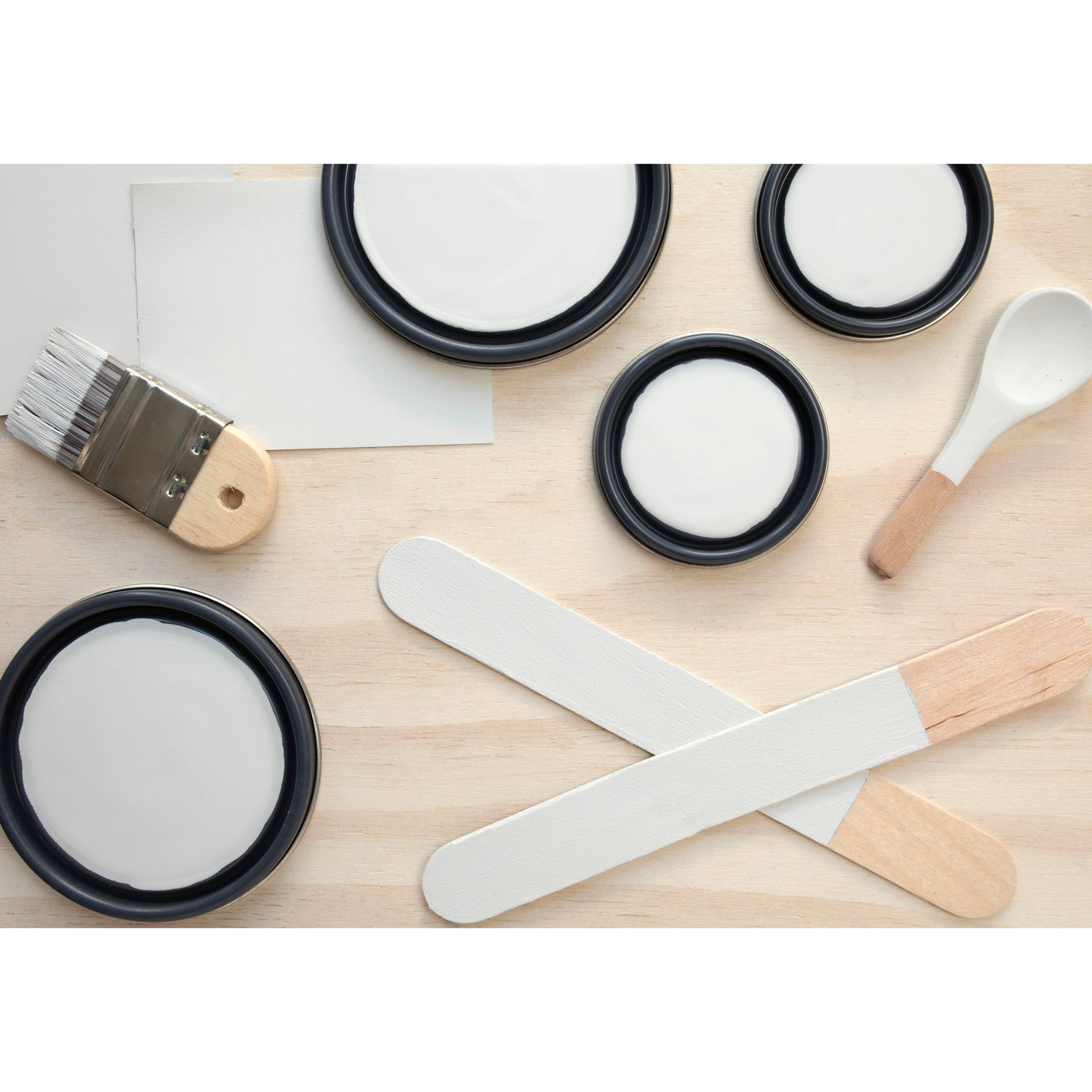 flatlay with paint lids, small paint brush, wooded spoons and rounded sticks painted in Chalky