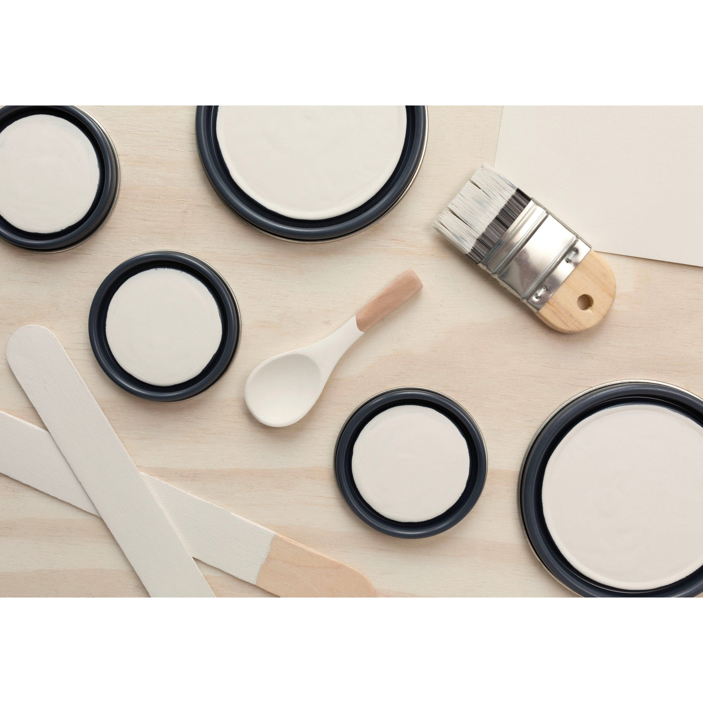 flatlay with paint lids, small paint brush, wooden spoons and rounded sticks painted in Historic White