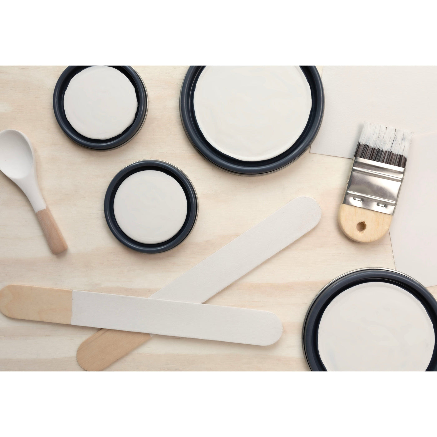 flatlay with paint lids, small paint brush, wooden spoons and rounded sticks painted in Crisp Muslin