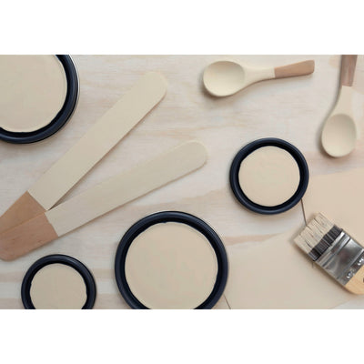 flatlay with paint lids, small paint brush, wooded spoons and rounded sticks painted in Buttercream Frosting