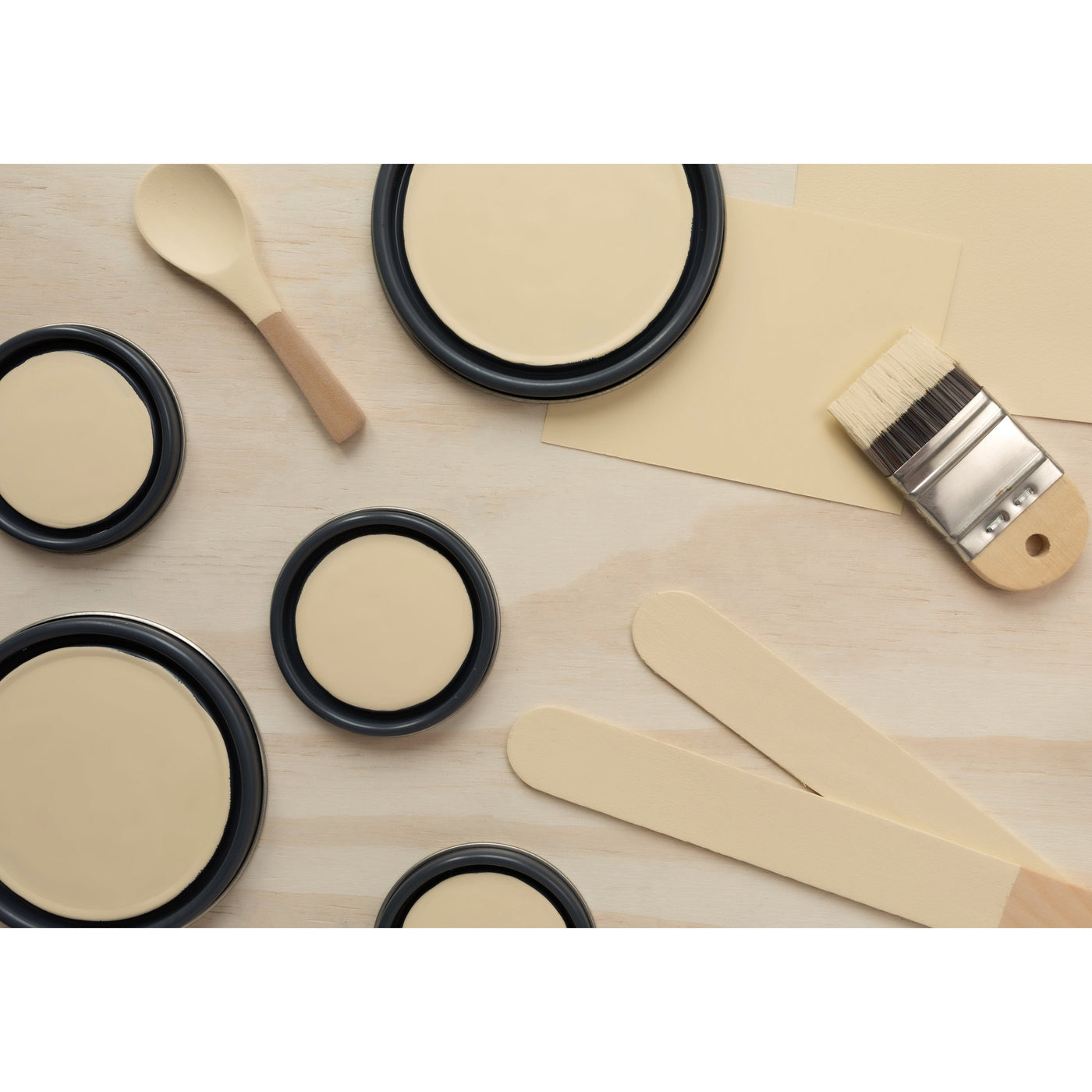 flatlay with paint lids, small paint brush, wooded spoons and rounded sticks painted in Creme Fraiche