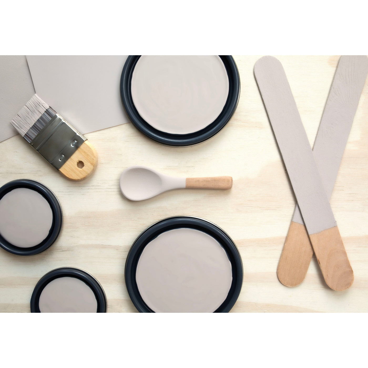 flatlay with paint lids, small paint brush, wooden spoons and rounded sticks painted in Desert Rock