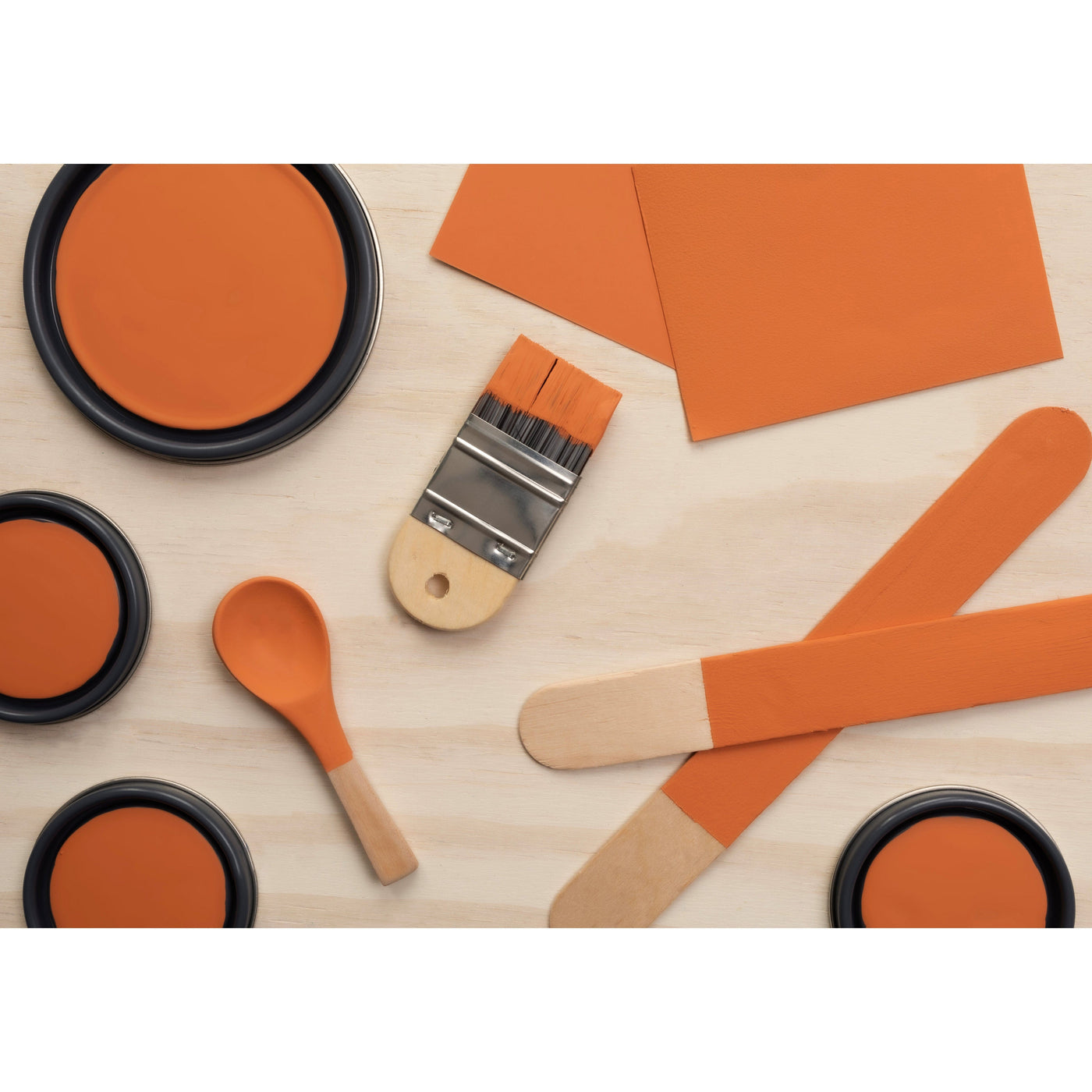  flatlay with paint lids, small paint brush, wooden spoons and rounded sticks painted in Deep Coral