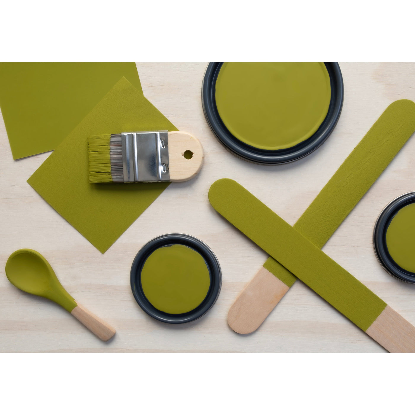 flatlay with paint lids, small paint brush, wooden spoons and rounded sticks painted in Gecko