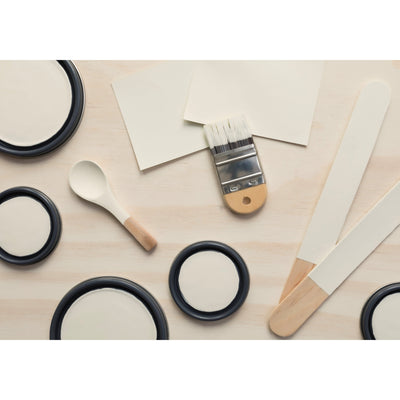 flatlay with paint lids, small paint brush, wooden spoons and rounded sticks painted in  Glisten Green