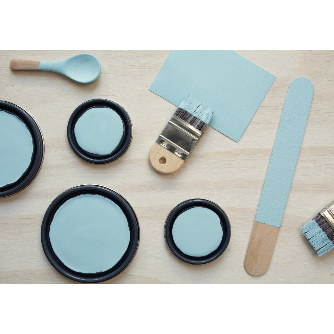 flatlay with paint lids, small paint brush, wooded spoons and rounded sticks painted in Blue Moon