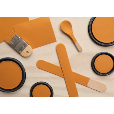 flatlay with paint lids, small paint brush, wooded spoons and rounded sticks painted in Cognac
