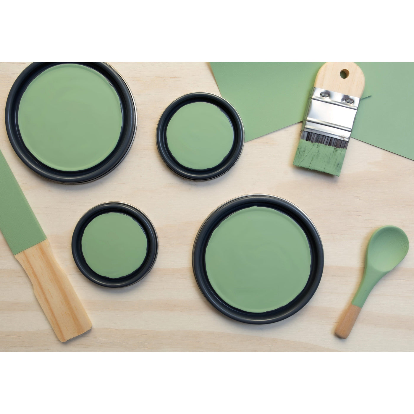 flatlay with paint lids, small paint brush, wooded spoons and rounded sticks painted in Cloistered Garden